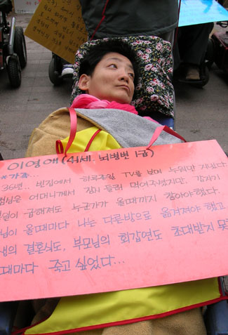 "비록 몸은 불편하지만..." 한 여성 장애인이 움직이지 않는 몸을 휠체어에 기댄 채 집회에 참가하고 있다.