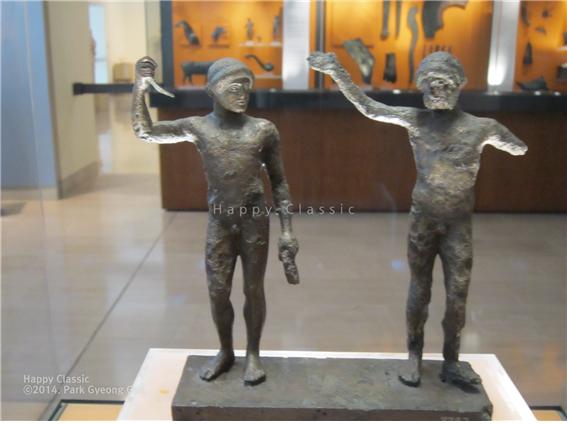 오른쪽에 있는 나이든 남성이 왼쪽의 청년의 우승을 선언하고 있는 모습을 표현한 조각, 청년이 왼손에 아령(halteres)을 들고 있는 것으로 보아 그가 멀리뛰기에 출전했던 것으로 추정된다. 델피 고고학 박물관 ⓒ박경귀