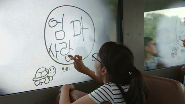 통학버스에 구현된 ‘스케치북 윈도우’ 기술을 이용해 창문에 글씨를 쓰고 있는 어린이의 모습.ⓒ현대자동차그룹