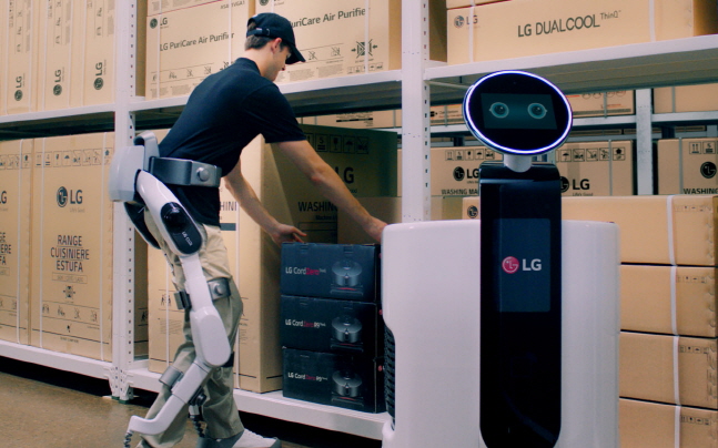 'LG 클로이 수트봇'을 착용한 작업자가 물류센터에서 상품을 쇼핑카트로봇에 옮겨담고 있다.ⓒLG전자