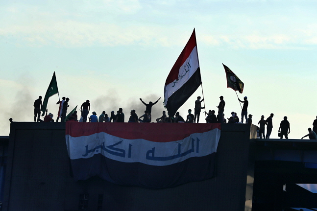 이라크 수도 바그다드의 타흐리르 광장 인근 건물에서 반정부 시위대가 국기를 흔들며 시위를 벌이고 있다.ⓒ뉴시스