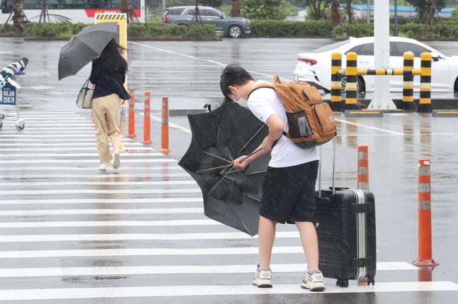 제14호 태풍 '찬투(CHANTHU)'가 북상 중인 14일 오후 제주국제공항 내 렌터카 터미널에서 한 관광객이 힘겹게 우산을 펼치고 있다.ⓒ뉴시스