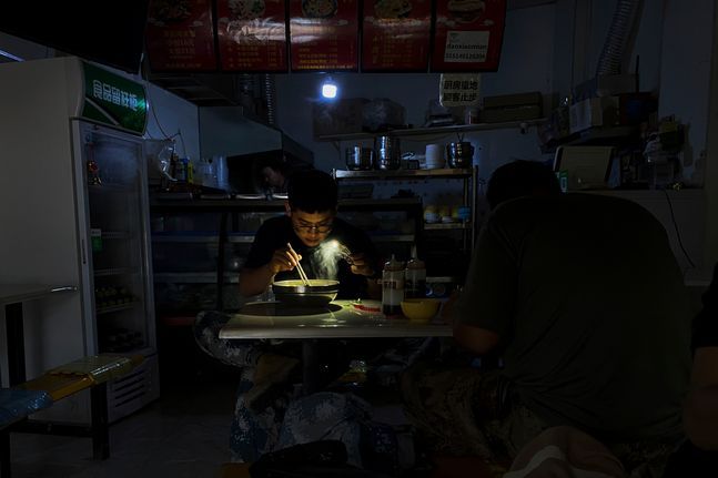지난달 29일 중국 북동부 랴오닝성 선양의 한 식당에서 한 손님이 정전으로 스마트폰 손전등을 사용해 국수를 먹고 있다.ⓒAP/뉴시스