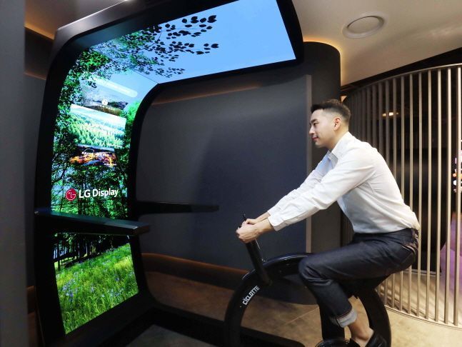 LG디스플레이 직원이 대형 유기발광다이오드(OLED) 스크린과 운동기구를 합친 콘셉트 제품 ‘버추얼 라이드’를 체험하고 있다.ⓒLG디스플레이
