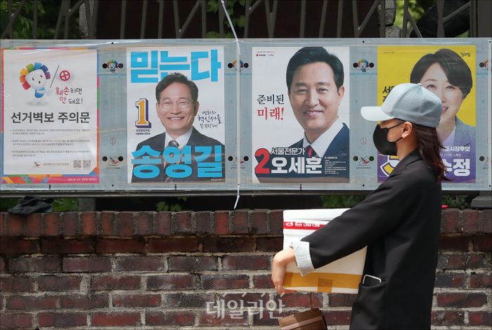 6.1 전국동시지방선거 공식 선거운동이 시작된 지난 19일 서울 종로구의 한 길가에 부착된 서울시장 후보들의 선거 벽보 앞으로 한 시민이 길을 지나고 있다. ⓒ데일리안 홍금표 기자