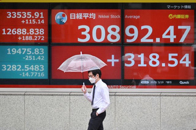 19일 일본 닛케이225지수가 표시된 도쿄 거리의 전광판 앞을 한 남성이 우산을 쓰고 지나가고 있다. ⓒ AFP/연합뉴스